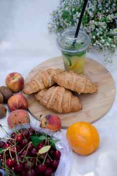 健康的野餐夏天一天羊角面包新鲜的水果柠檬水桃子樱桃猕猴桃橙子白色野花