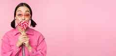 时尚的朝鲜文女孩舔萝莉波普吃糖果微笑站太阳镜粉红色的背景