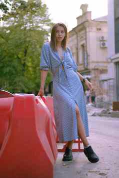 金发女郎女孩长蓝色的衣服小黑色的手提包肩膀摆姿势红色的护栏走城市完整的长度拍摄