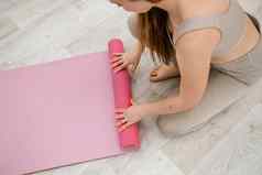 年轻的女人卷粉红色的健身瑜伽席锻炼锻炼首页生活房间瑜伽工作室健康的习惯适合重量损失概念特写镜头照片