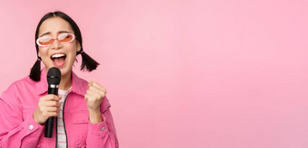 快乐美丽的亚洲女孩唱歌小麦克风享受卡拉ok摆姿势粉红色的工作室背景