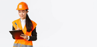 很高兴亚洲女建设工程师架构师采取笔记剪贴板写作检查建筑区域穿安全头盔女商人检查工人