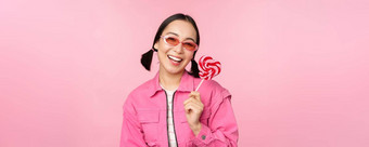 时尚的朝鲜文女孩舔<strong>萝莉</strong>波普吃糖果微笑站太阳镜粉红色的背景
