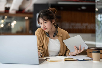 微笑亚洲年轻的女耳机移动PC屏幕听学习在线课程快乐业务女人耳机视频调用客户服务