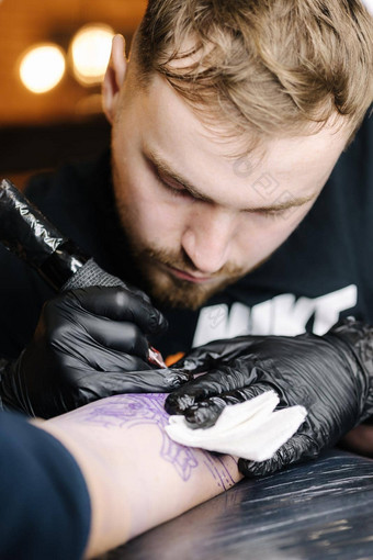 关闭纹身主使黑色的纹身油漆主作品黑色的无菌手套年轻的纹身艺术家工作