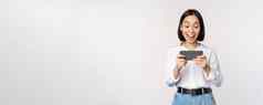 图像年轻的亚洲女人看智能手机应用程序持有移动电话屏幕笑微笑站白色背景