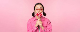 时尚的朝鲜文女孩舔<strong>萝莉</strong>波普吃糖果微笑站太阳镜粉红色的背景