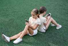 漂亮的女孩相同的衣服电话体育地面运动场孩子们冲浪互联网智能手机上瘾先进的现代孩子们社会网络
