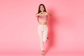 时尚美生活方式概念完整的长度卡哇伊卖弄风情的亚洲女孩富有魅力的衣服显示心手势表达爱同情护理站粉红色的背景