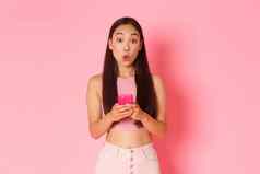 技术沟通在线生活方式概念感兴趣亚洲时尚的女孩逗乐特殊的提供互联网商店持有移动电话撅嘴好奇的粉红色的背景