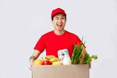 在线购物食物交付互联网商店概念友好的微笑亚洲快递红色的帽t恤持有包杂货店交付眨眼客户给客户端产品包