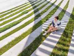 女人发短信智能手机坐在板凳上城市公园条纹影子绿色草坪上现代生活方式千禧一代