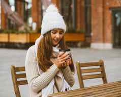 美丽的年轻的女孩喝咖啡茶塑料杯子秋天冬天女人长头发温暖的衣服坐着街咖啡馆温暖热喝