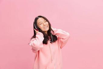 放松亚洲年轻的夫人粉红色的连帽衫运动衫可爱的耳机听最喜欢首歌关闭眼睛摆姿势孤立的粉红色的工作室背景好提供声音流媒体平台概念