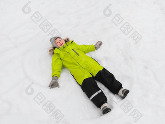 笑男孩绿色连身裤使雪天使形状雪快乐的孩子玩在户外雪天气前视图快乐孩子色彩斑斓的西装