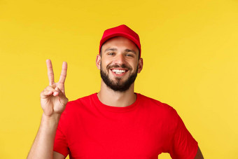 特写镜头友好的快乐的有胡子的交付的家伙显示和平标志穿红色的统一的帽t恤快递喜欢采取护理<strong>客户</strong>订单安全购物包裹转移黄色的<strong>背景</strong>