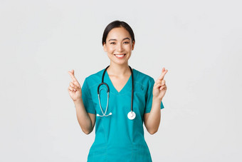 科维德医疗保健工人流感大流行概念乐观微笑亚洲女医生医生实习医生风云信仰交叉手指好运气使希望白色背景