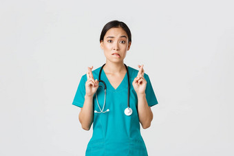 科维德医疗保健工人流感大流行概念充满希望的紧张亚洲女实习生实习医生风云等待新闻医生交叉手指咬唇相机祈祷