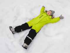 微笑男孩绿色连身裤使雪天使形状雪快乐的孩子玩在户外雪天气前视图快乐孩子色彩斑斓的西装