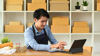 年轻的亚洲男人。检查在线订单数字平板电脑准备包裹盒子交付客户电子商务在线销售概念