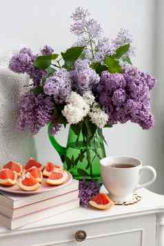 香花束色彩斑斓的紫丁香站绿色玻璃花瓶白色背景杯热茶切片葡萄柚