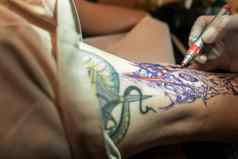 特写镜头手拉丁纹身艺术家标记草图纹身男人的腿标记