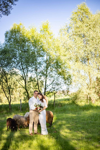 快乐年轻的人婚礼服装站草地背景羊羔草地