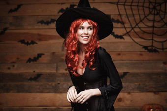万圣节女巫概念快乐万圣节红色的头发女巫持有摆姿势木工作室背景