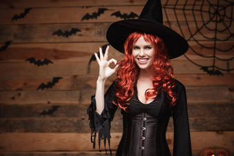 万圣节女巫概念快乐万圣节红色的头发女巫持有标志手指摆姿势木工作室背景