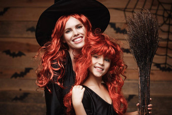 美丽的高加索人妈妈。女儿长红色的头发女巫服装庆祝万圣节摆姿势蝙蝠蜘蛛网络<strong>木工</strong>作室背景
