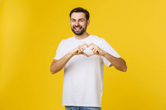 微笑年轻的男孩使心手势胸部白色衬衫孤立的黄色的背景