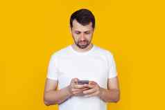 年轻的男人。胡子白色t恤持有手智能手机信息互联网自然表达式站孤立的黄色的背景