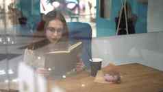 年轻的女人坐在玻璃咖啡馆阅读书女孩喝咖啡