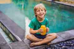 男孩喝多汁的奶昔芒果玻璃梅森Jar钢稻草背景池健康的生活概念复制空间