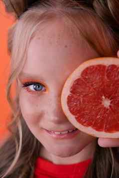 年轻的女孩葡萄柚片橙色背景卷曲的头发马尾辫