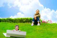 微笑女孩坐纸板盒子滑动山植物花园妈妈。笑了笑看起来快乐童年概念