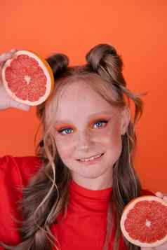 年轻的女孩葡萄柚片橙色背景卷曲的头发马尾辫