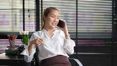 满意年轻的员工坐着工作场所会说话的手机