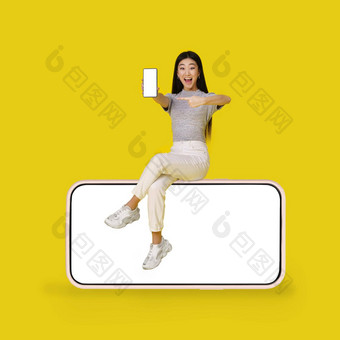 亚洲年轻的女孩持有智能手机坐着<strong>巨</strong>大的<strong>巨</strong>大的智能手机黑色的屏<strong>幕</strong>孤立的黄色的背景模拟产品放置应用程序广告复制空间