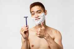 美人卫生概念很高兴好看的亚洲男人。推荐剃须刀剃须奶油显示翘拇指微笑很高兴脸奶油站白色背景