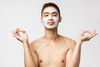 美护肤品水疗中心概念肖像放松年轻的亚洲男人。面部嫩肤面具化妆品产品冥想使Zen标志瑜伽和平享受住首页