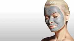 美丽的女人应用白色面部面具美治疗水疗中心女孩应用粘土面部面具灰色背景