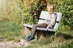 迷人的男孩平静地坐着木板凳上城市公园