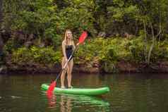 站桨董事会女人桨登机湖站快乐paddleboard蓝色的水行动拍摄年轻的女人桨董事会