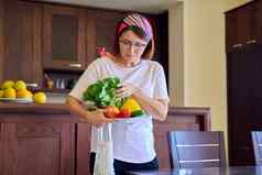 中间岁的女人首页厨房新鲜的蔬菜网纺织生态袋