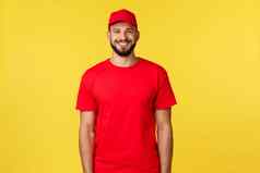 表达邮件交付包转移物流概念英俊的友善的快递红色的统一的公司t恤帽微笑广泛的站黄色的背景