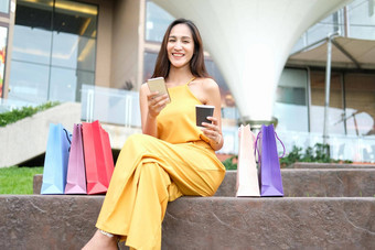 女人持有咖啡杯智能手机购物袋消费主义生活方式购物中心