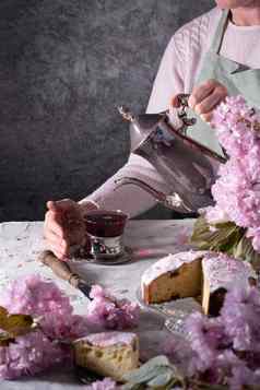 女人倒茶银茶壶背景粉红色的樱花花复活节