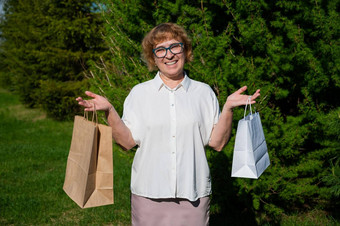 快乐上了年纪的女人站公园持有纸袋退休购物狂享受购物概念生态友好的产品<strong>保护环境</strong>