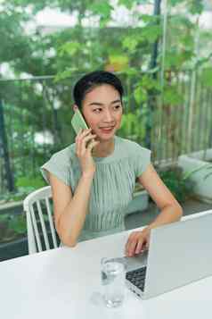 年轻的亚洲女企业家会说话的电话工作首页办公室